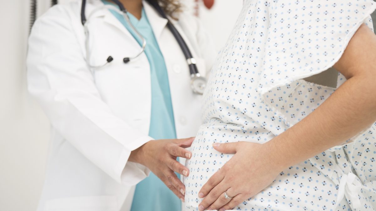 Mixed race doctor examining pregnant patient's belly